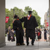 Two students wearing caps and gowns celebrate commencement on Main Campus